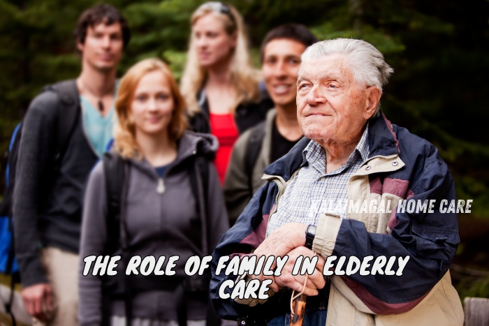 An elderly man, smiling and dressed in a casual jacket, stands in a scenic outdoor setting surrounded by his supportive family. This image highlights the importance of family involvement in elderly care, as emphasized by Kalaimagal Home Care in Coimbatore. The diverse group of family members, including young adults, are seen in the background, demonstrating a united and loving presence in caring for their elder.